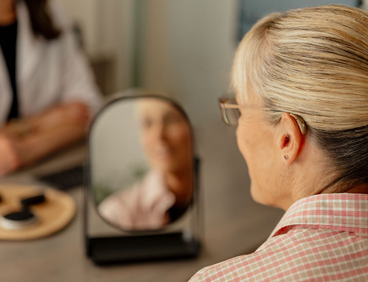Woman trying on new hearing aids in the mirror.