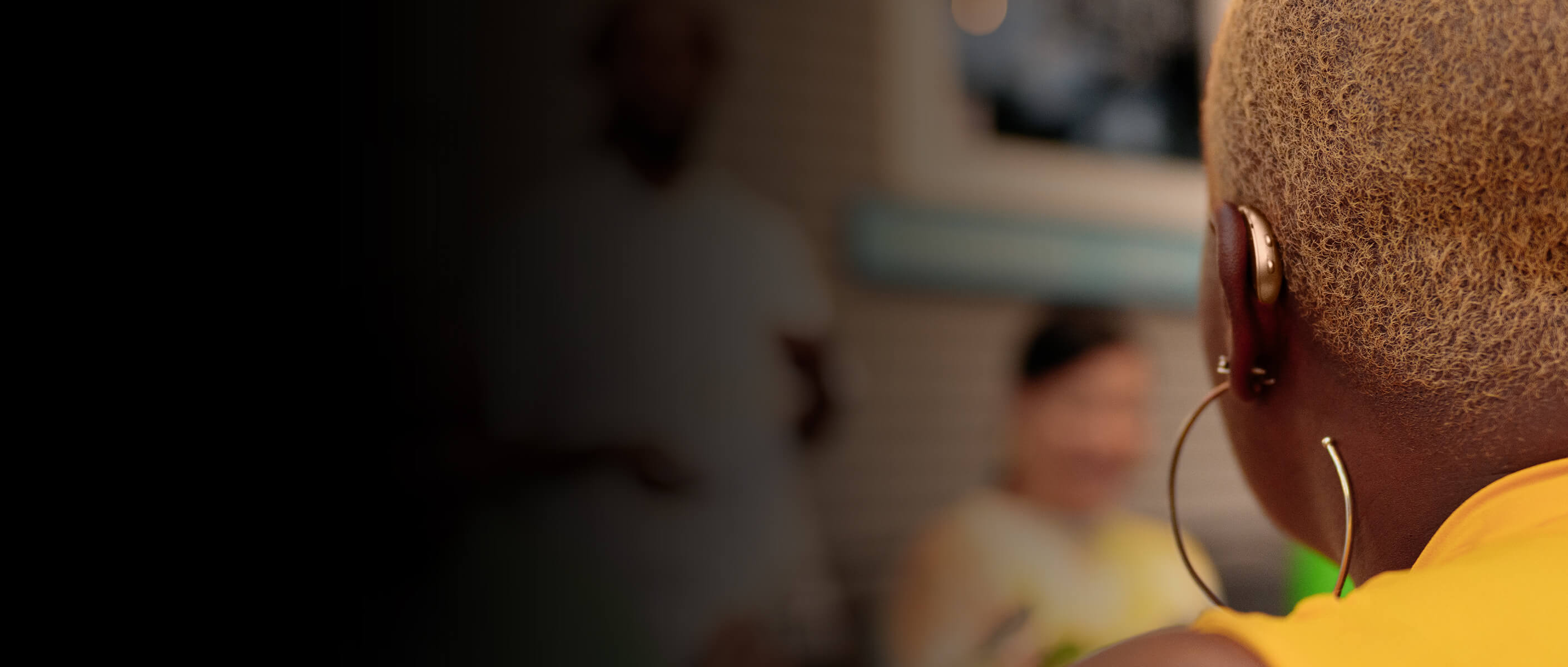 woman in a yellow shirt from behind wearing a bronze hearing aid